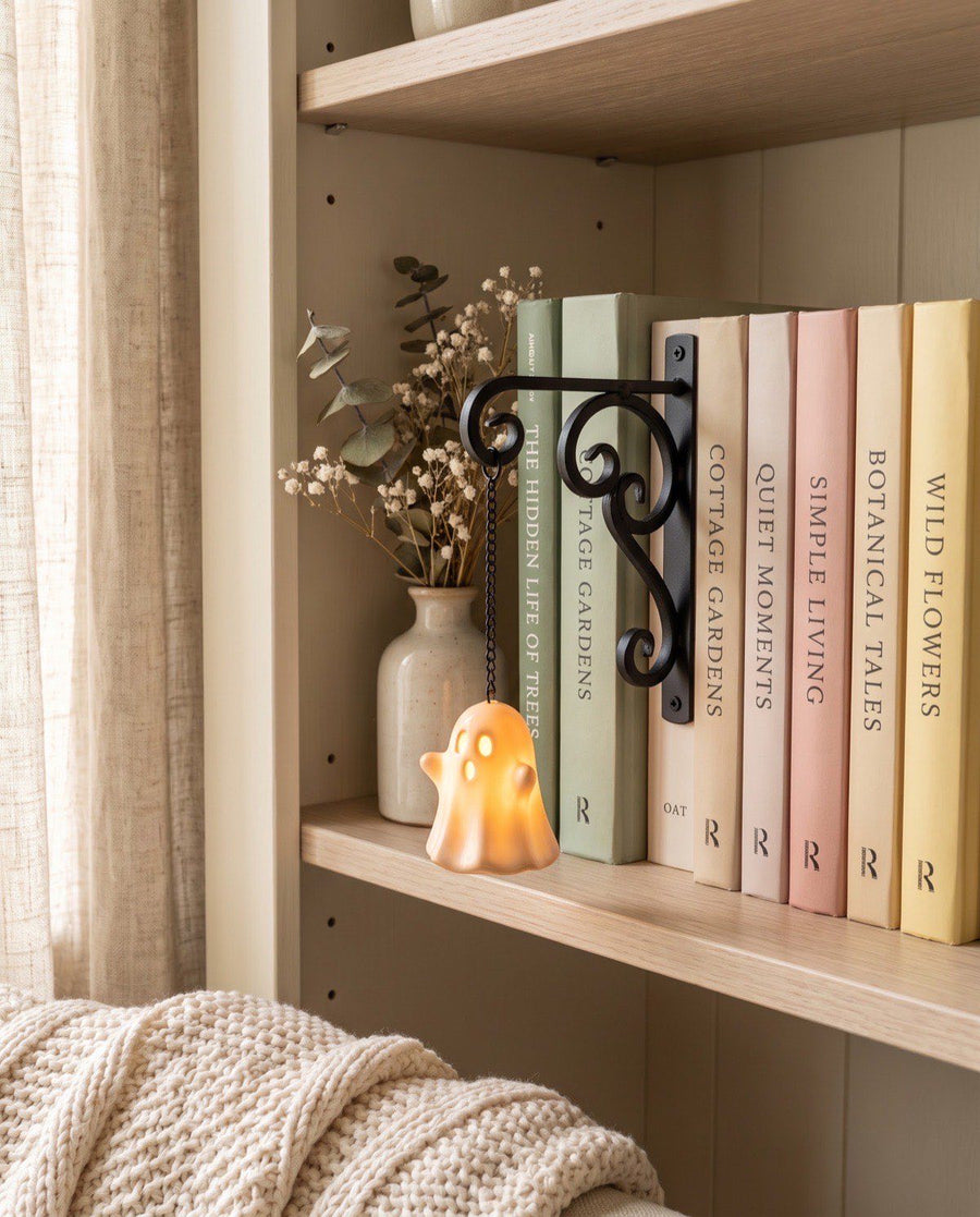 A NookPalace shelf lantern glowing on a pale oak bookshelf in a cosy reading nook